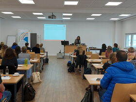 Teilnehmende im Veranstaltungsraum von hinten mit Blick auf Leinwand