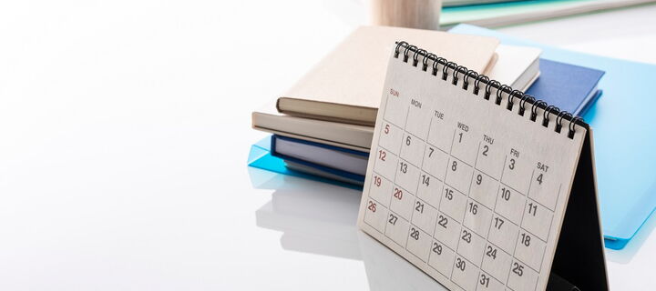 stehender Kalender mit Monatsansicht auf Schreibtsich mit Büchern und Stiftehalter im Hintergrund
