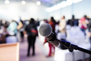 Nahaufnahme eines Mikrofons, stehende Personen und Plenum im Hintergrund