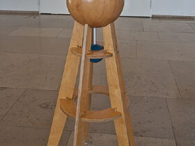 Eine Holzkugel mit Stöpseln auf einem Podest ist zu sehen.