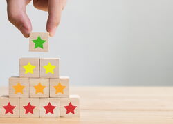 Hand setzt Holzbausteine mit farbigen Sternen zu einer Pyramide auf
