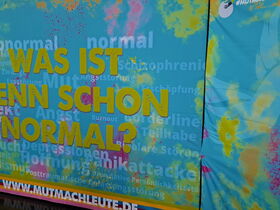 Stellwand zur Ausstellung der Mutmachleute. Schriftzug Was ist denn schon normal? auf buntem Hintergrund