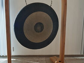 Eine Klangscheibe, die in einem Holzbogen hängt und mit beiliegenden Schlägeln in Schwingung versetzt wird