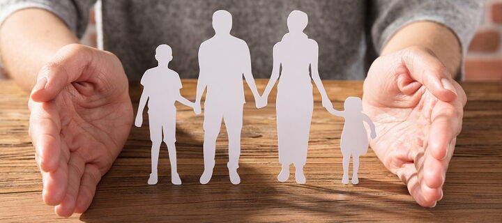 Scherenschnitt einer Familie auf Tisch, geschützt durch zwei Hände